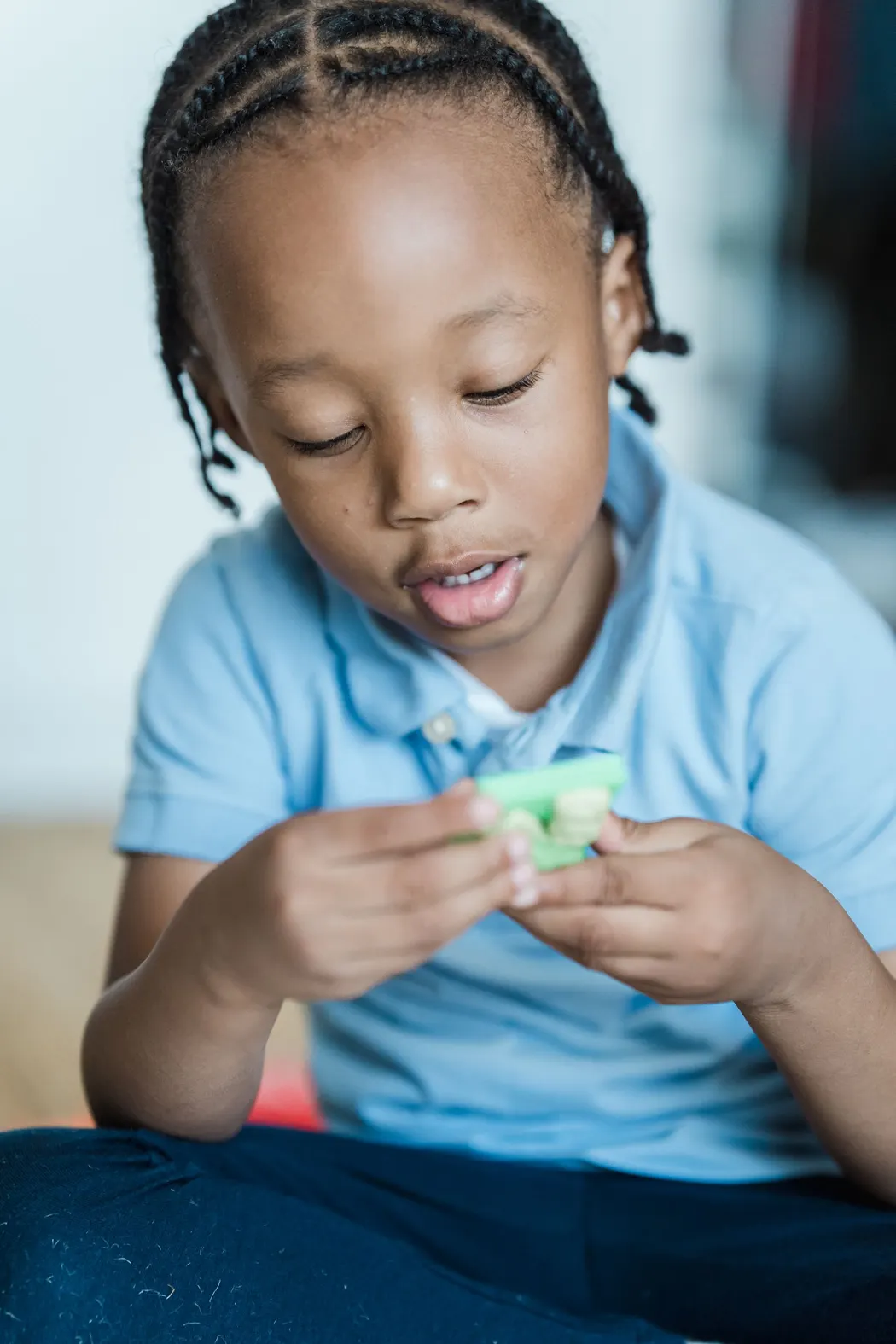A young boy in a light blue polo shirt looking closely at a small green learning material in his hands
