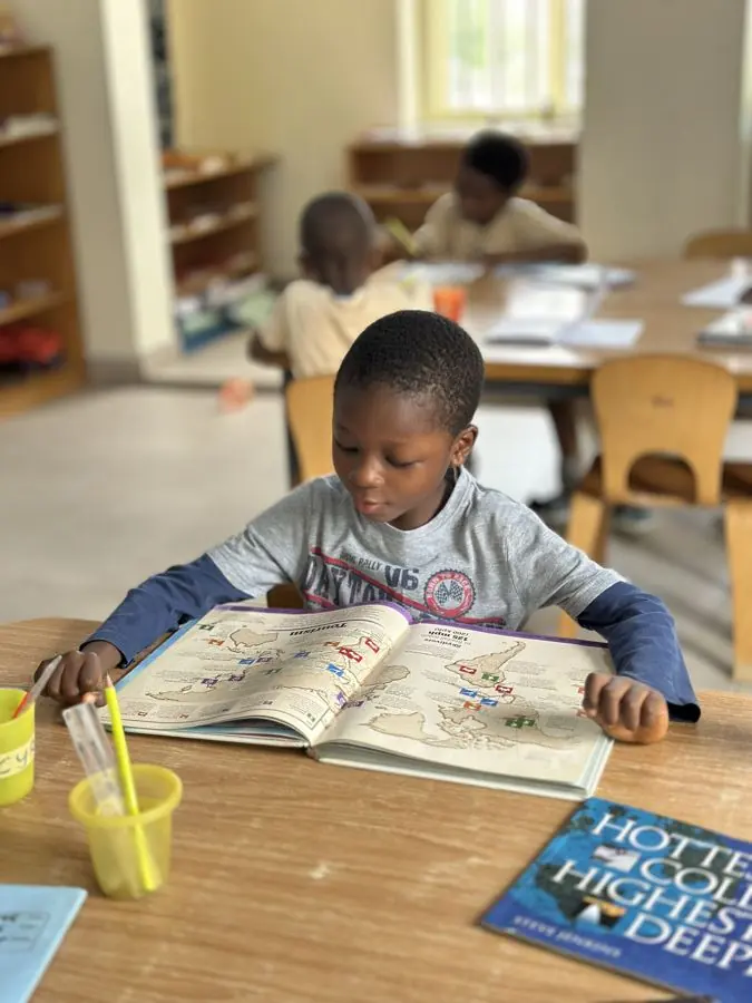 A boy reading a large picture book at a classroom table