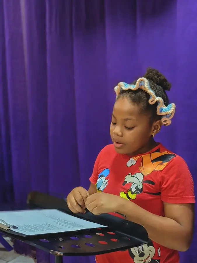 A girl reading aloud from a music stand in front of a purple backdrop