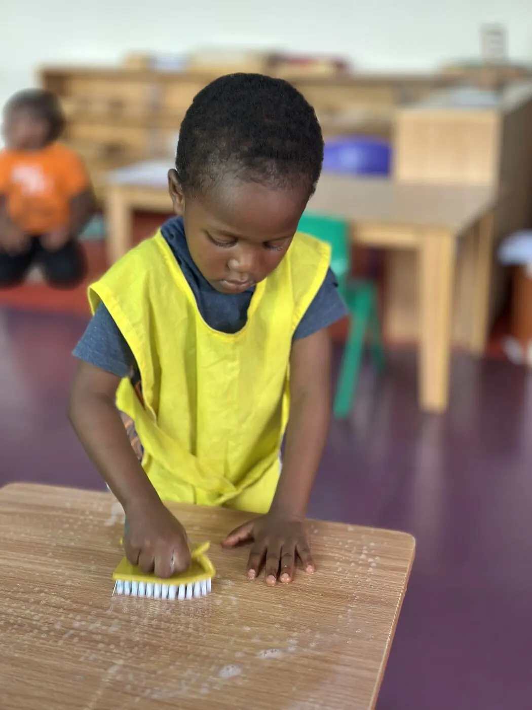 A toddler scrubbing a table during practical life work