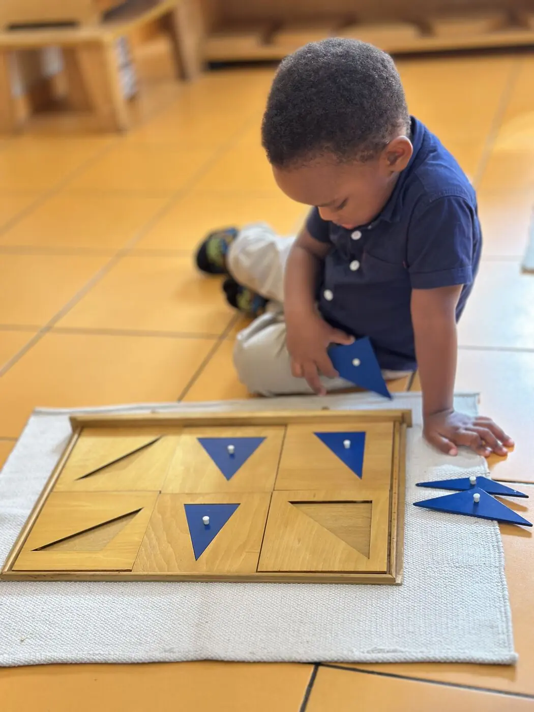 A young child fitting blue triangles into a Montessori geometric material on a floor mat