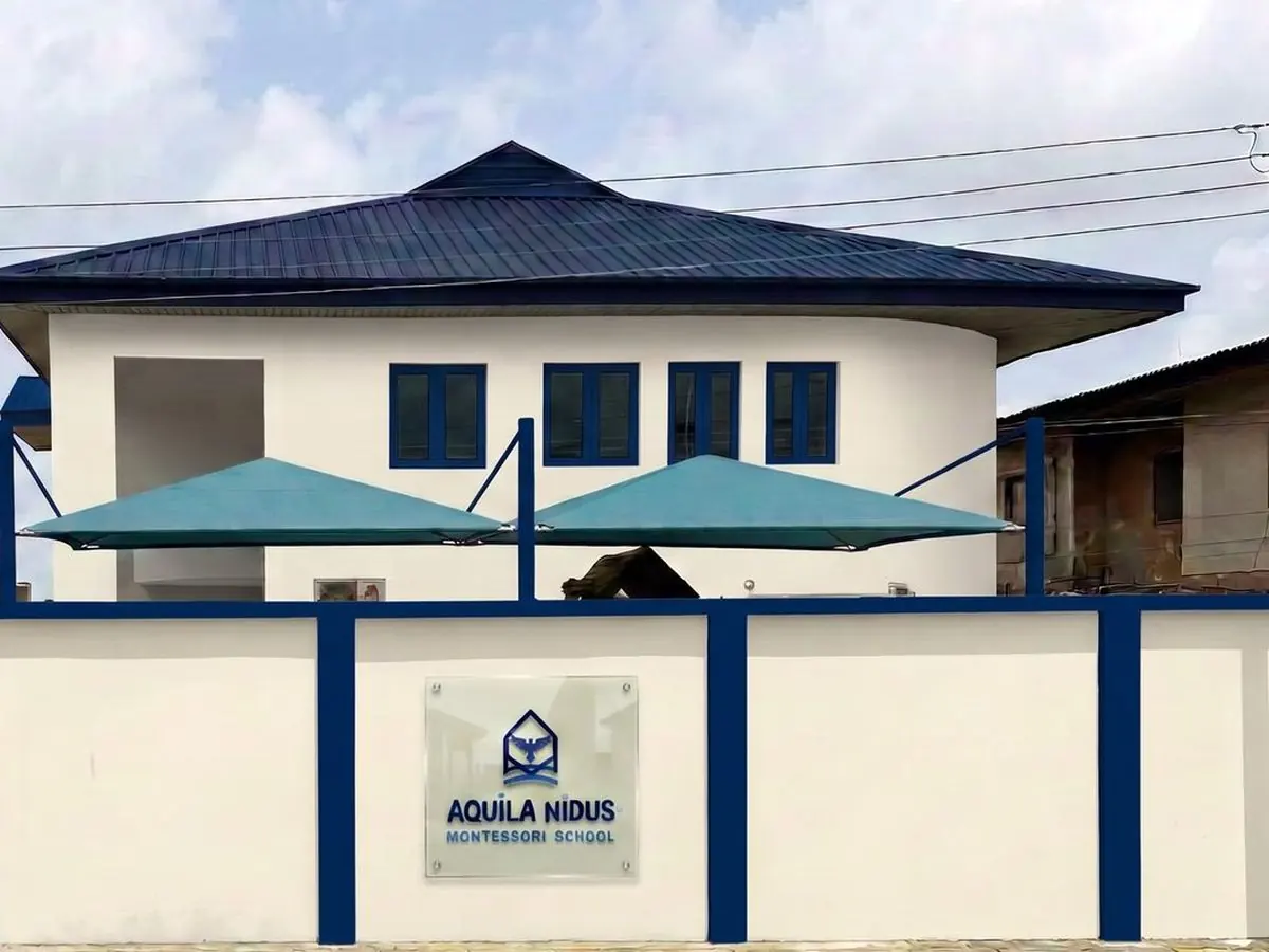 The Aquila Nidus Montessori School building behind its blue and white entrance wall and name sign