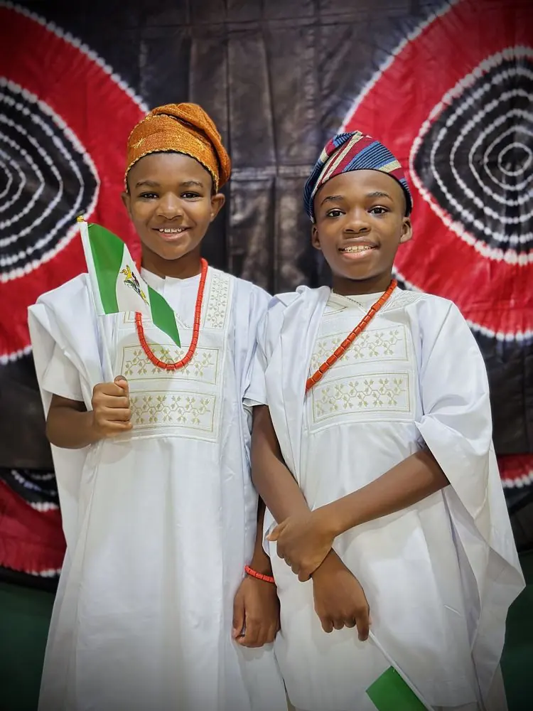 Two children in white traditional outfits holding Nigerian flags